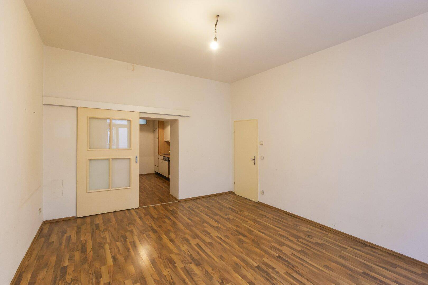 Leeres Zimmer mit Laminatboden und einer Schiebetür, die zu einem weiteren Raum führt.