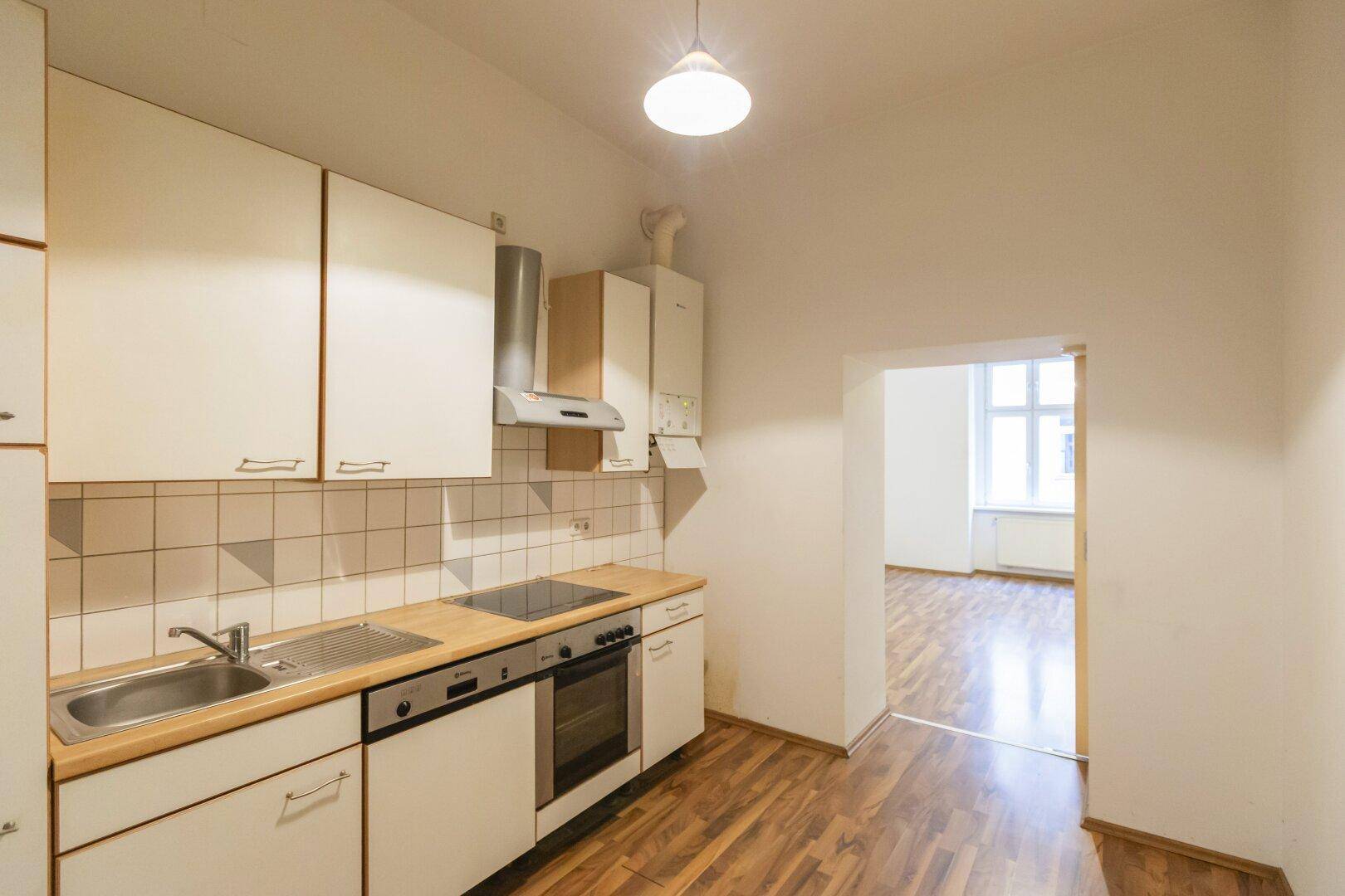 Helle Küche mit Einbauschränken, Holz-Arbeitsplatte und Blick in den angrenzenden Raum.