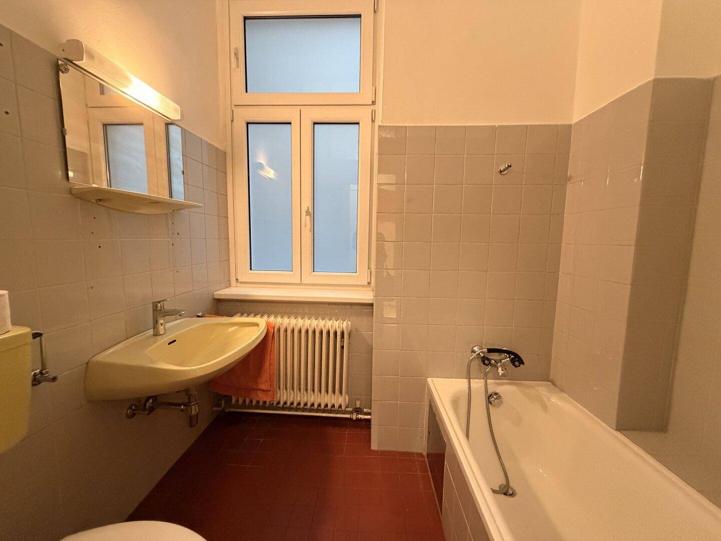 Badezimmer mit Badewanne, Waschbecken und Fenster, das eine Modernisierung benötigt.