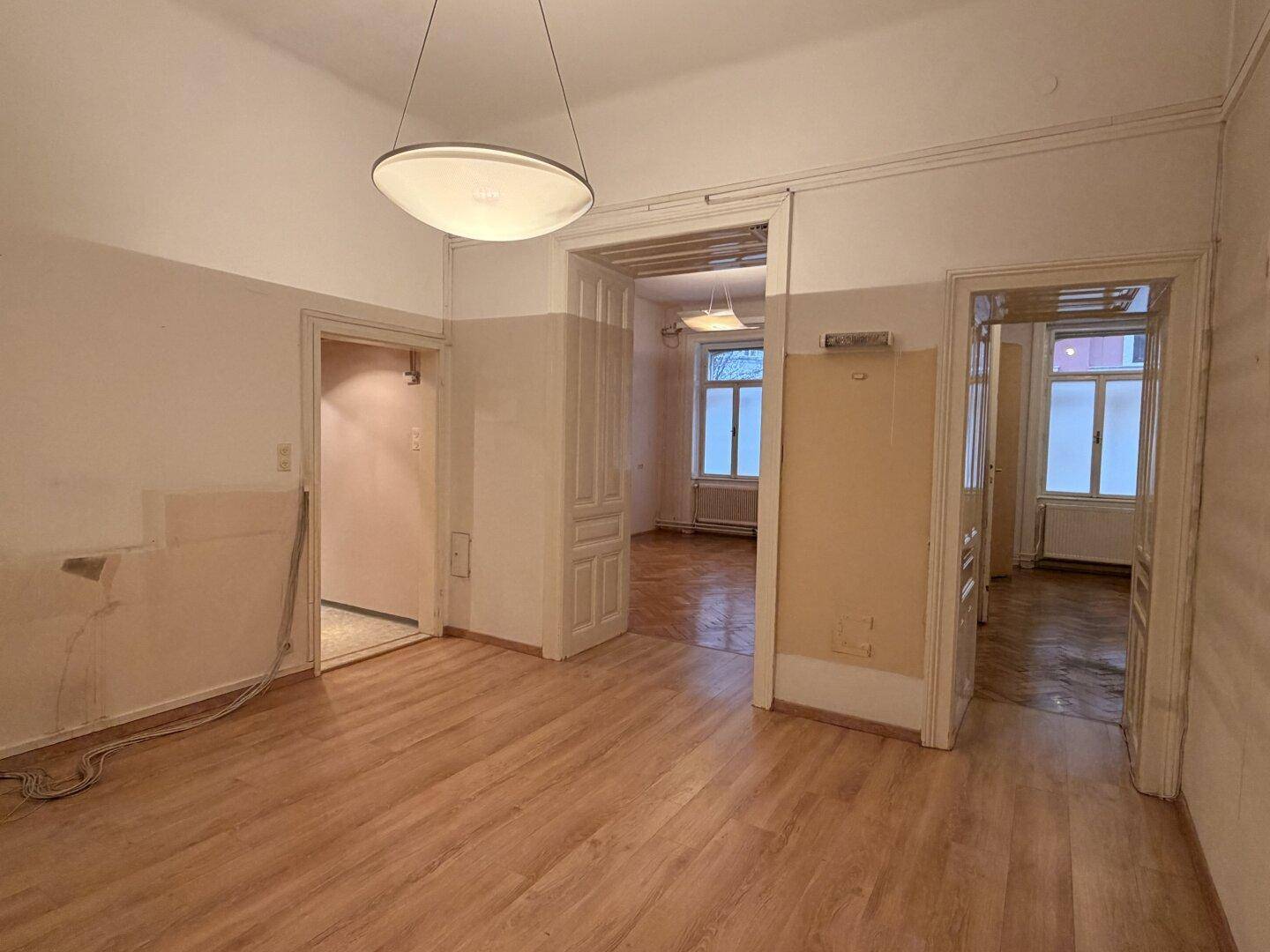 Geräumiger Raum mit Laminatboden und hohen Decken, der auf eine Renovierung wartet.