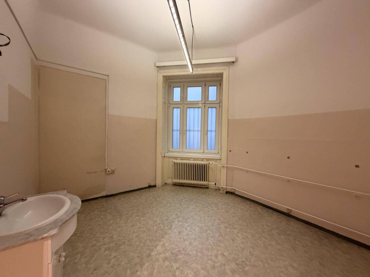 Raum mit Waschbecken, Fenster und Linoleumboden, der eine umfassende Renovierung benötigt.