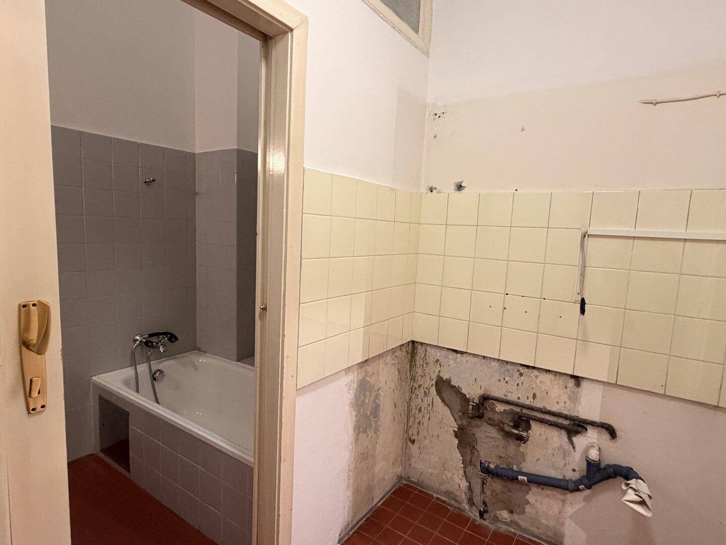 Badezimmer mit Badewanne und Fliesen, das deutliche Anzeichen von Renovierungsbedarf zeigt.