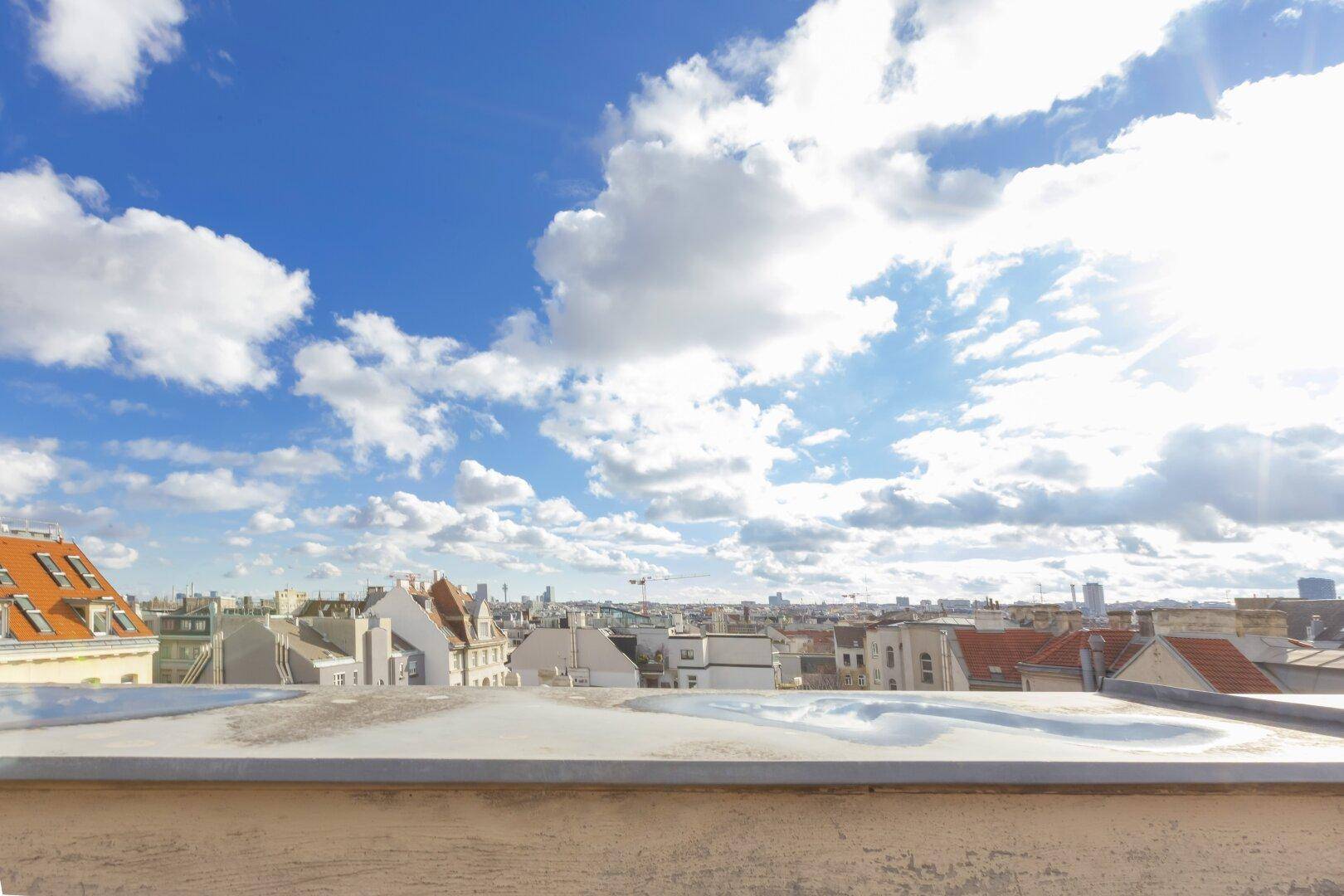 Weitläufiger Blick über die Dächer der Stadt unter einem strahlend blauen Himmel mit vielen Wolken.