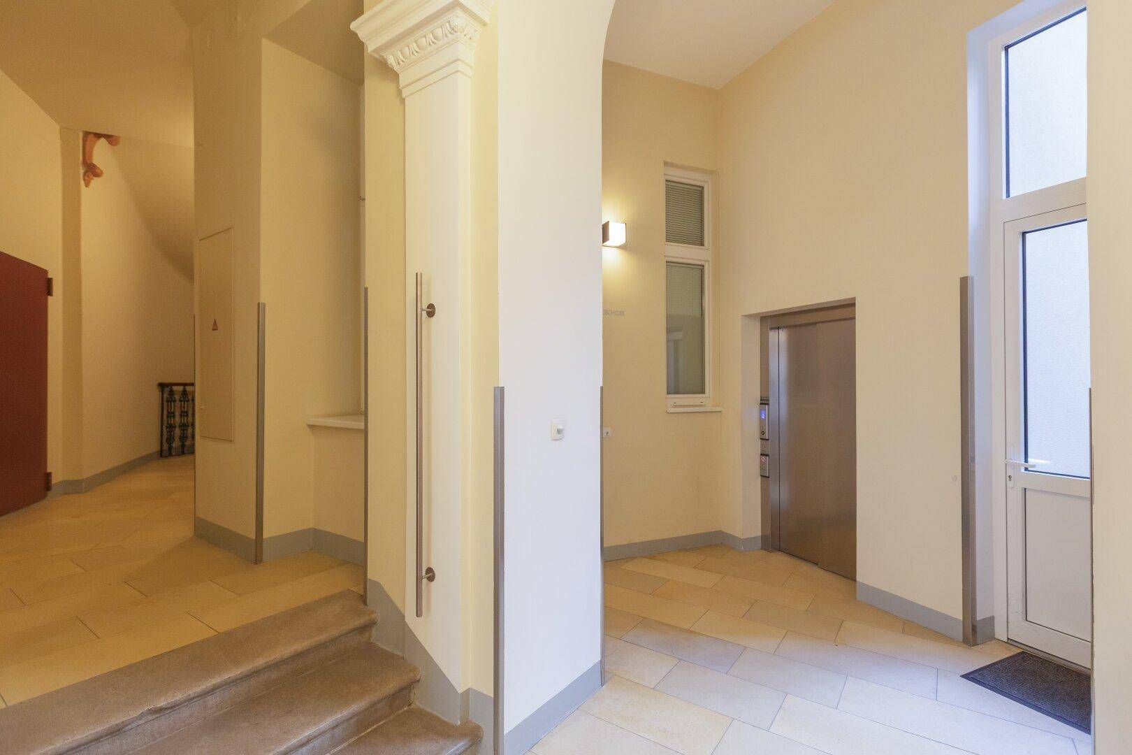 Heller Eingangsbereich mit Fliesenboden, hohen Decken und Zugang zum modernen Aufzug.