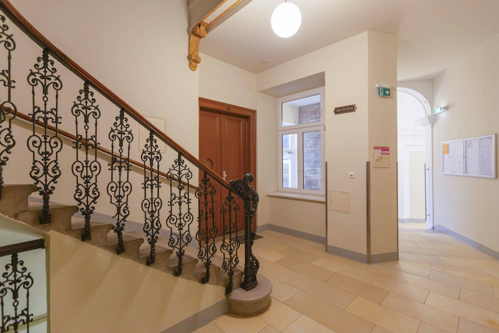Geräumiges Treppenhaus mit kunstvollem Geländer, hohen Decken und natürlichem Lichteinfall durch ein Fenster.