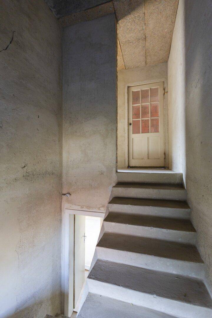 Treppenhaus mit einfachen Stufen und einer Holztür, die zu einem oberen Stockwerk führt.