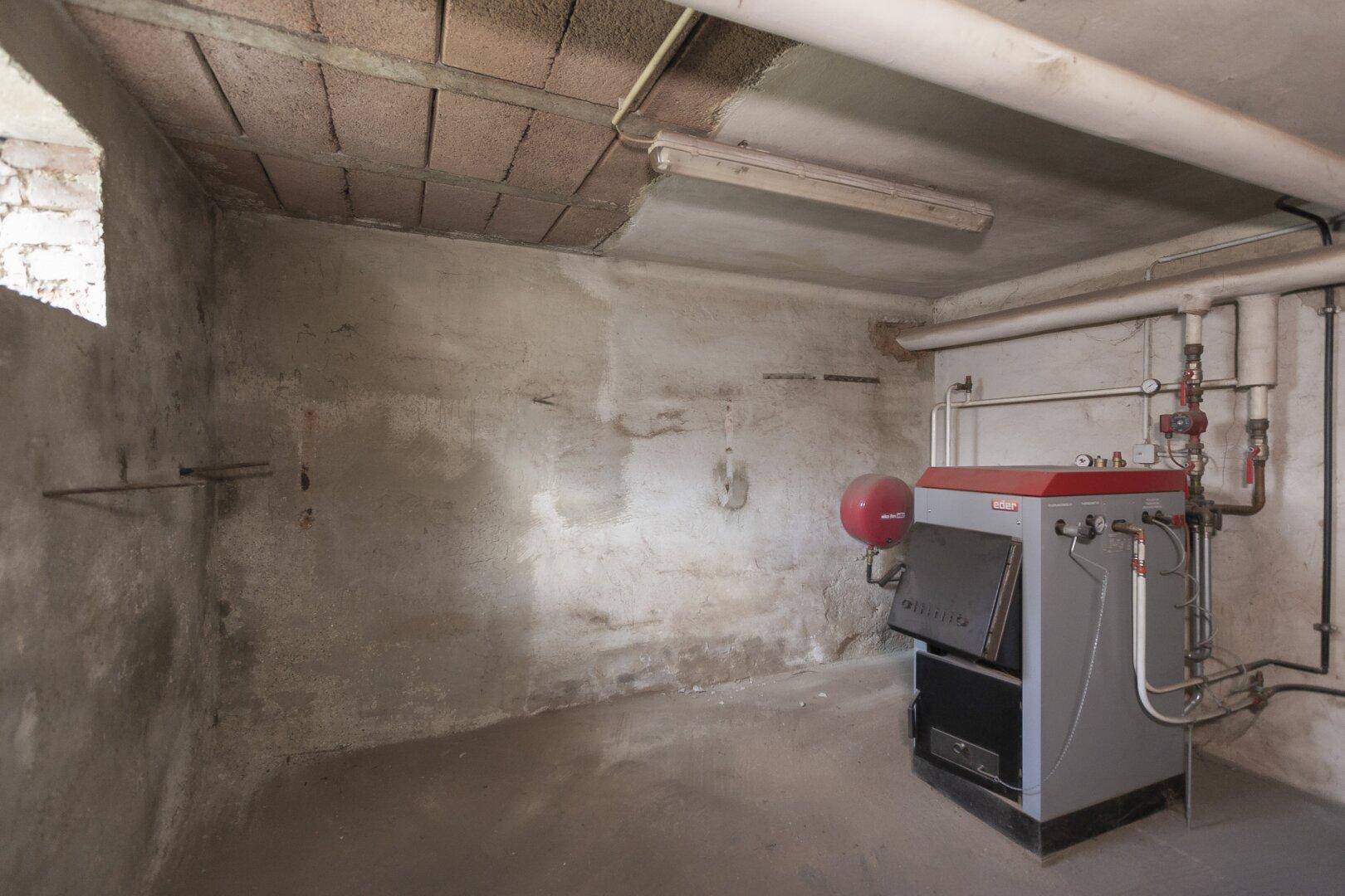 Heizungsraum im Keller mit einem alten Heizkessel und sichtbaren Rohrleitungen.