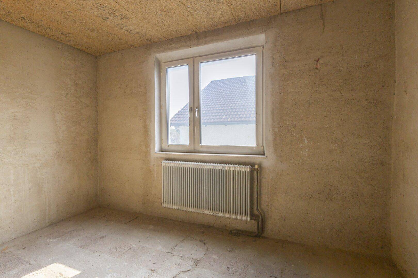 Unfertiger Raum mit einem Fenster und Heizkörper, bereit für den weiteren Ausbau.