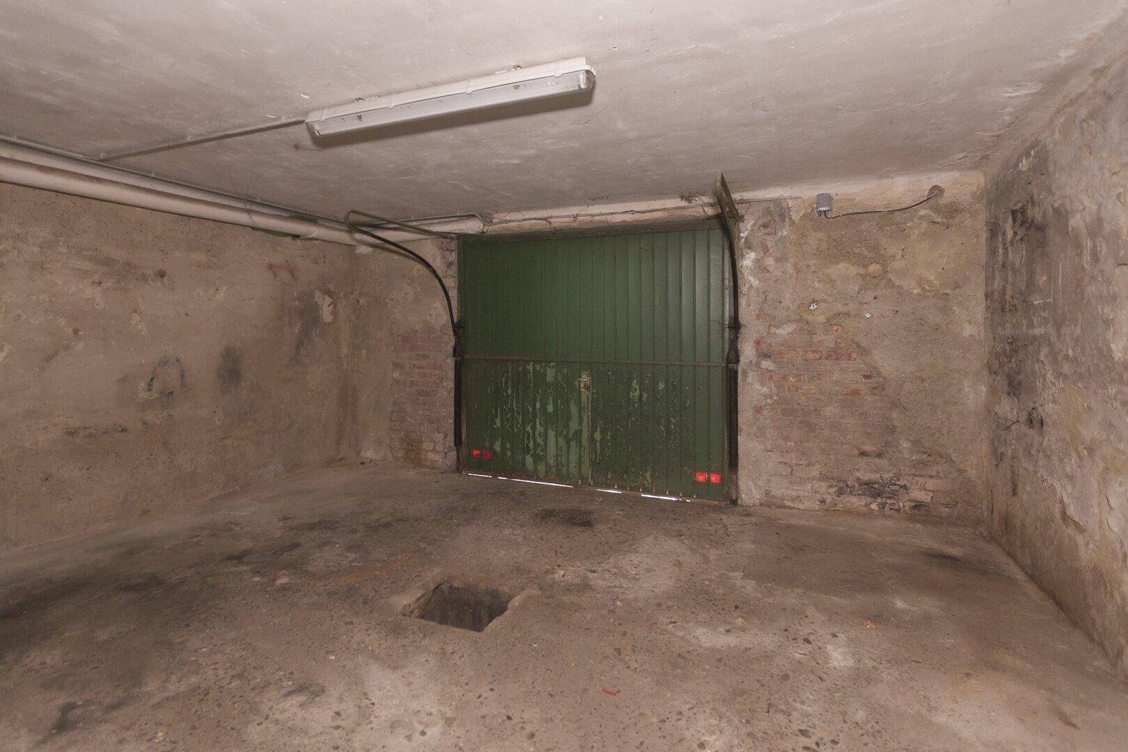 Einfache Garage im Kellergeschoss mit einem grünen Garagentor und Betonboden.