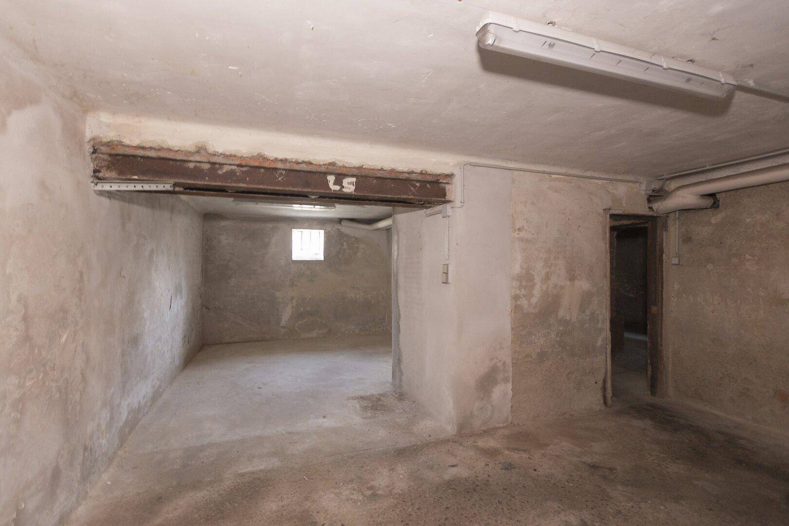 Geräumiger Kellerraum mit Betonboden und einem kleinen Fenster, ideal als Lagerfläche.