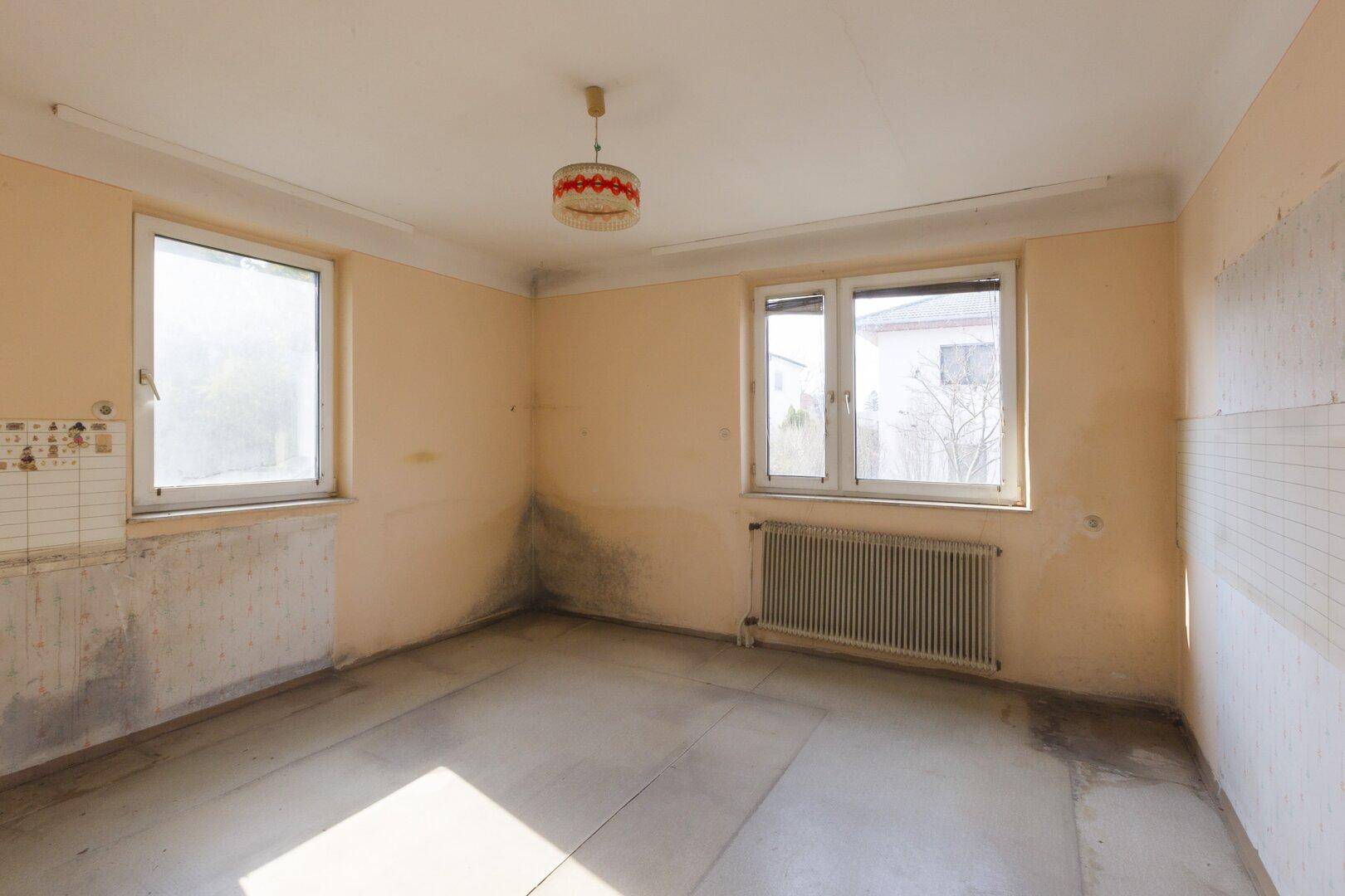Helles, unmöbliertes Zimmer mit zwei Fenstern und einem Heizkörper, bereit zur Renovierung.