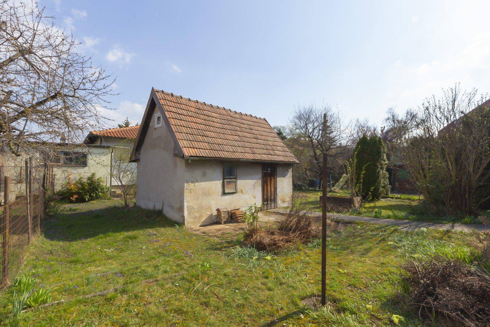 Kleines Gartenhaus mit Satteldach in einem verwilderten Garten mit altem Baumbestand.