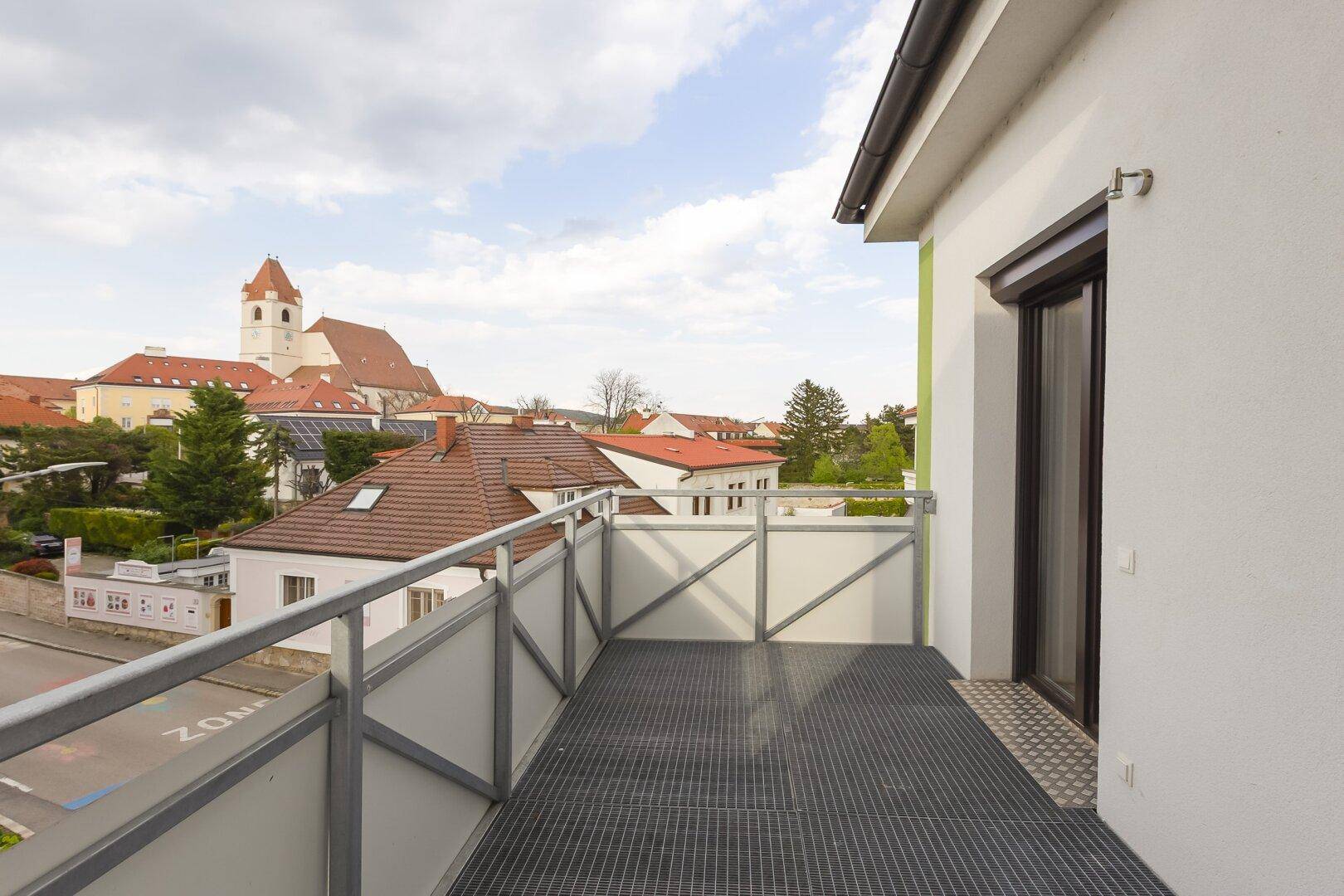 Geräumiger Balkon mit Metallgeländer und Blick auf die Stadt mit einer historischen Kirche im Hintergrund.