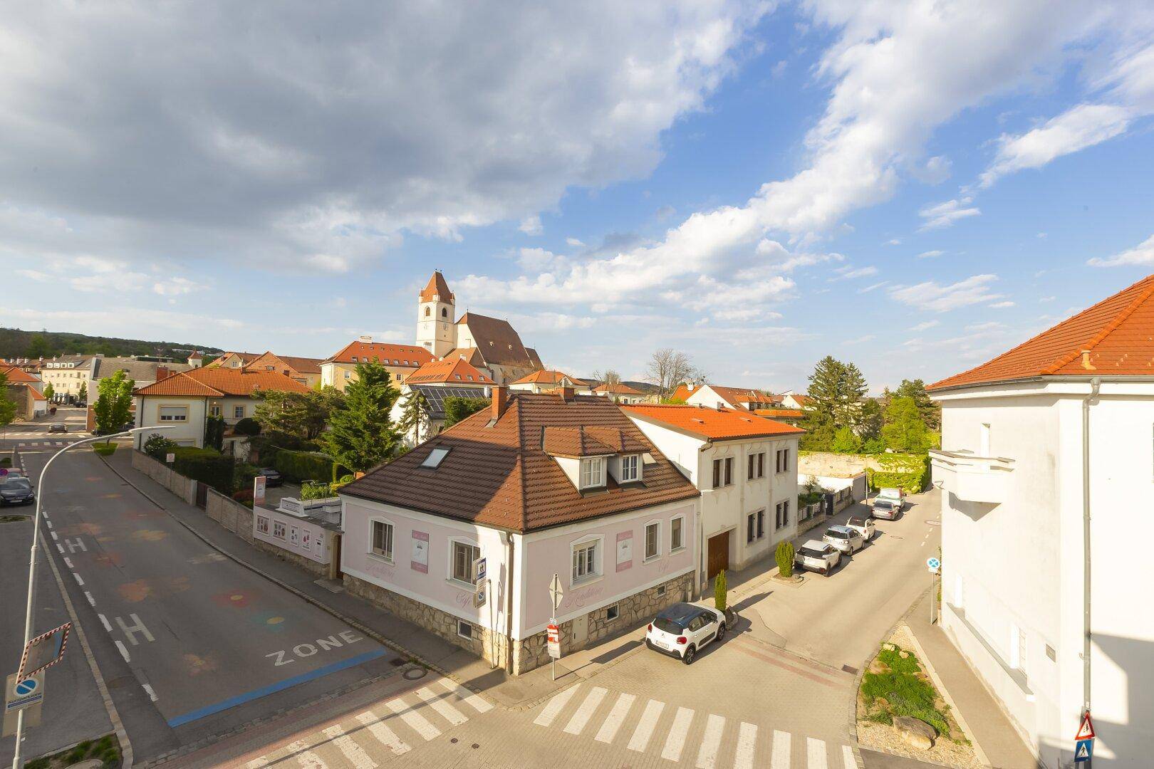 Panoramablick über eine Wohngegend mit traditionellen Häusern und einer Kirche im Hintergrund unter bewölktem Himmel.