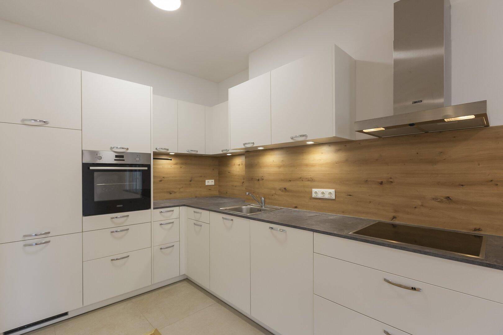 Moderne Einbauküche mit weißen Schränken, Holzrückwand und integrierten Edelstahlgeräten.