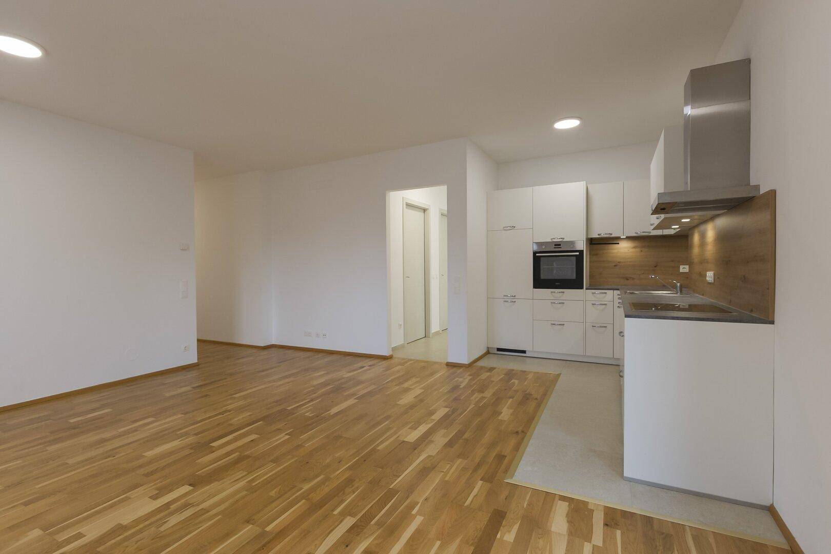 Moderner offener Wohnbereich mit integrierter Küche und Zugang zu einem Flur, ausgestattet mit Holzboden.