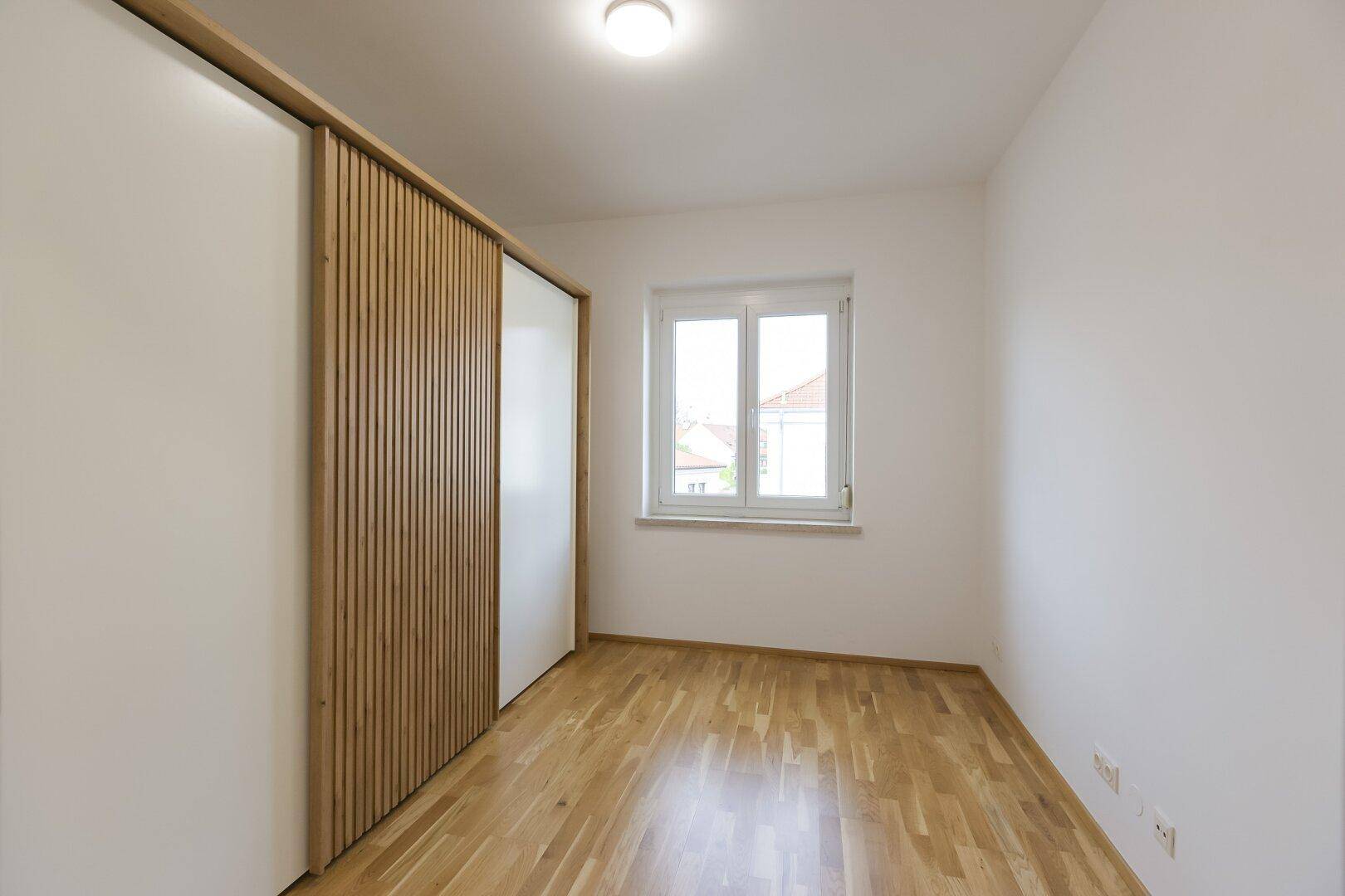 Schlafzimmer mit Holzboden, Fenster und praktischen Einbauschränken mit Holz- und Weißpaneelen.
