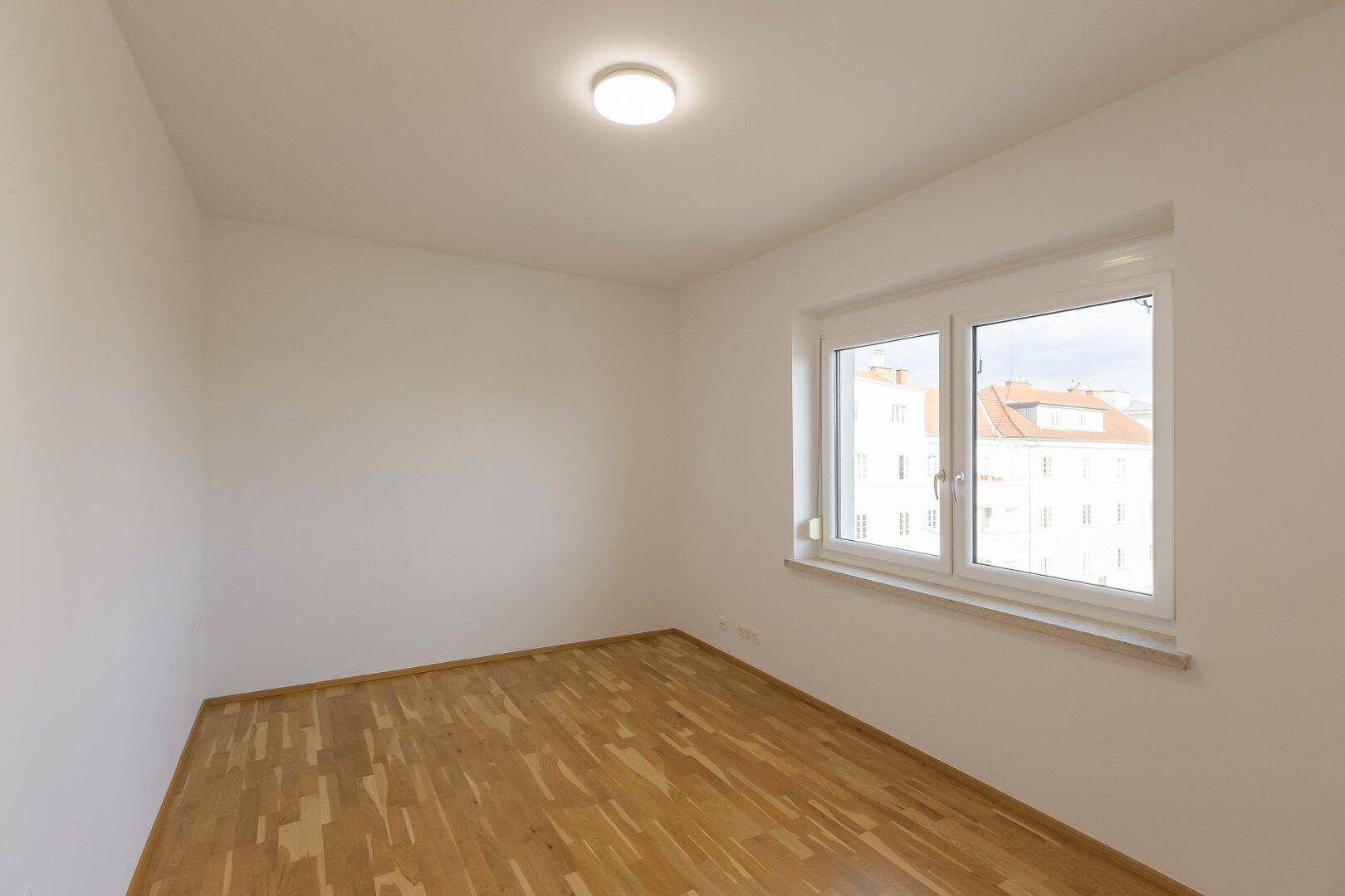 Helles Schlafzimmer mit Holzboden und einem großen Fenster, das viel Tageslicht hereinlässt.