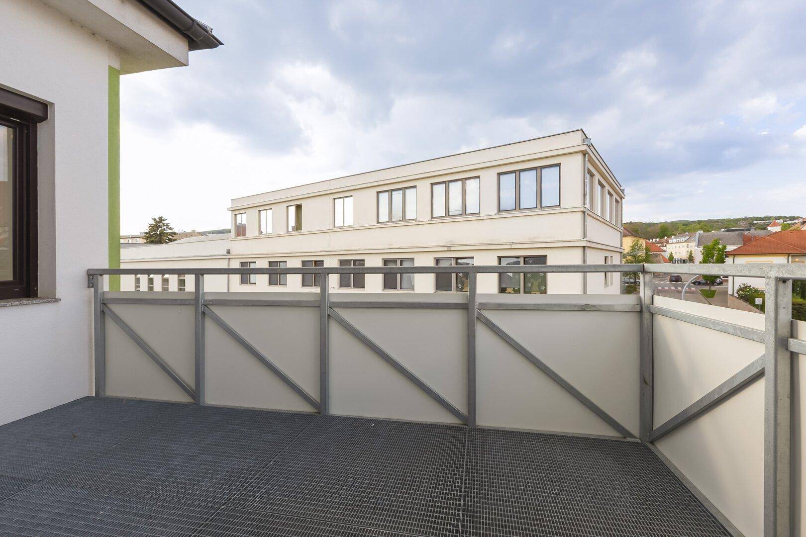 Geräumiger Balkon mit modernem Metallgeländer und Blick auf ein gegenüberliegendes Gebäude.