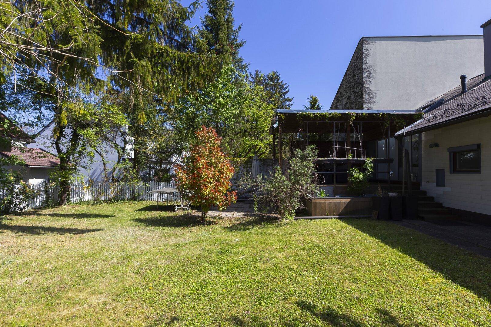 Weitläufiger Garten mit Rasenfläche, Bäumen und Blick auf die Gebäudefassade.