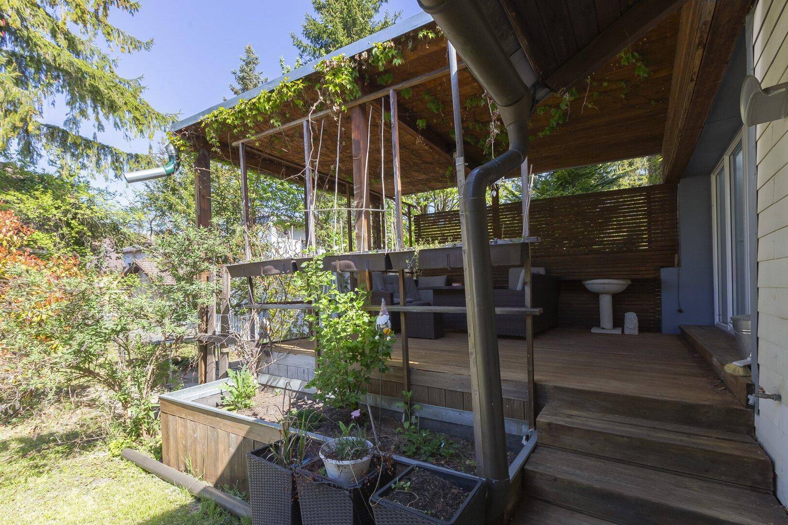 Gartenbereich mit Zugang zur überdachten Terrasse und kleinen Pflanzenbeeten.