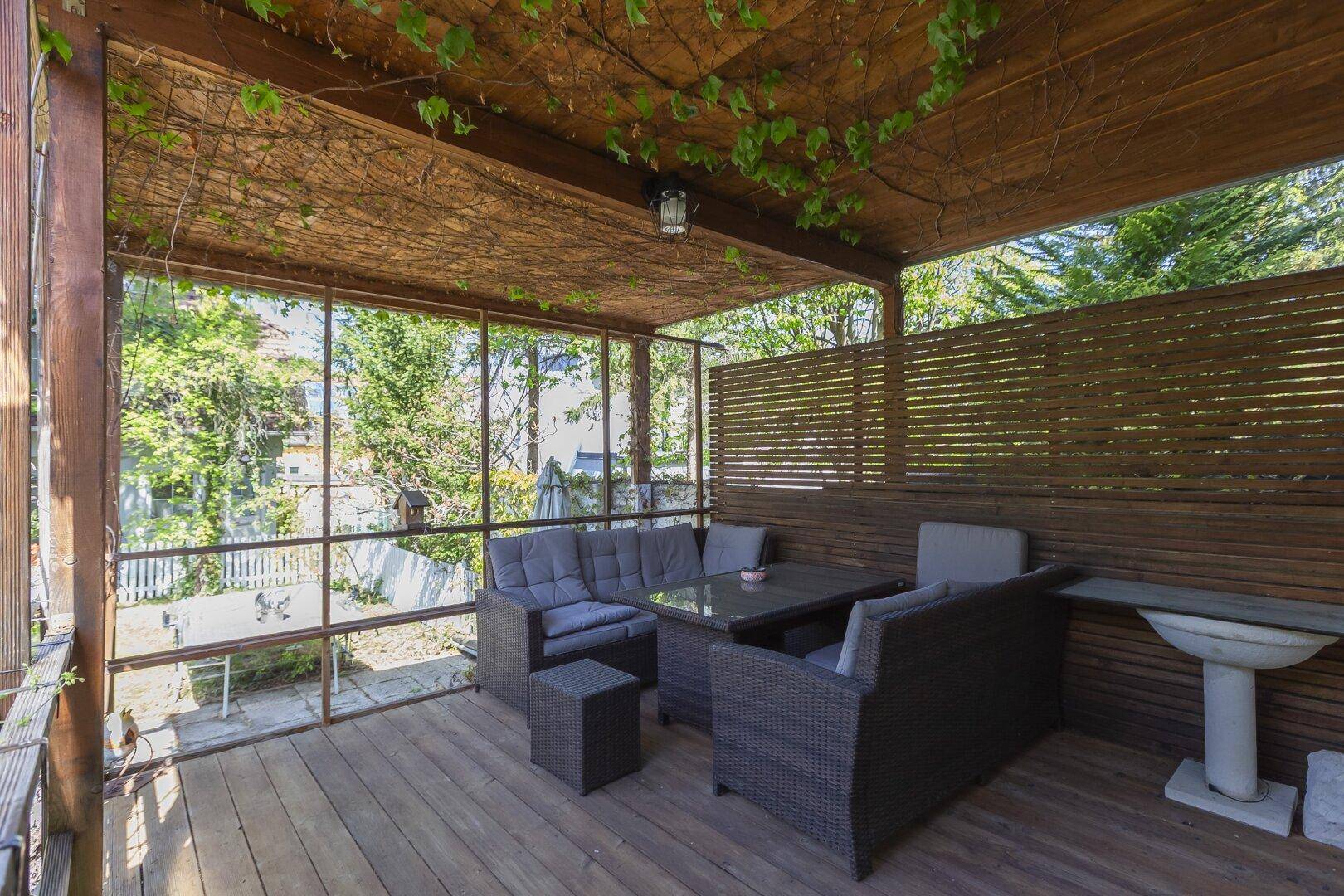 Überdachte Terrasse mit gemütlichen Loungemöbeln und Blick in den grünen Garten.