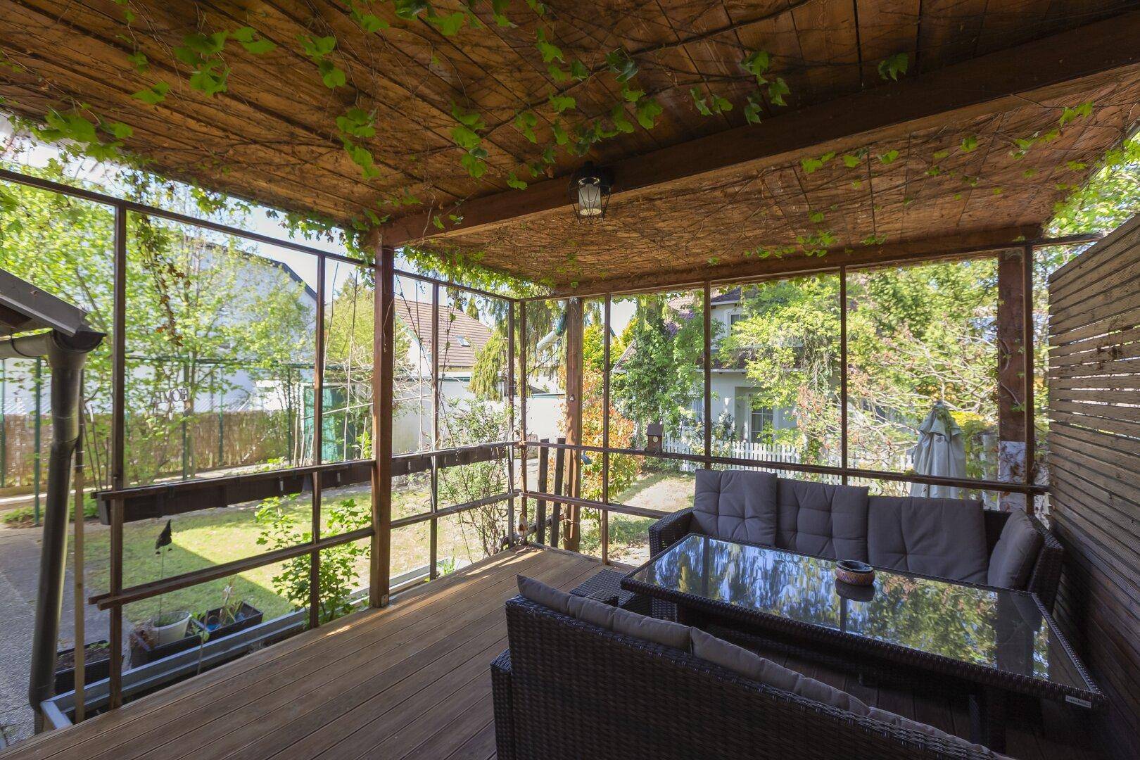 Überdachte Holzterrasse mit Loungemöbeln und weitem Blick in den Garten.