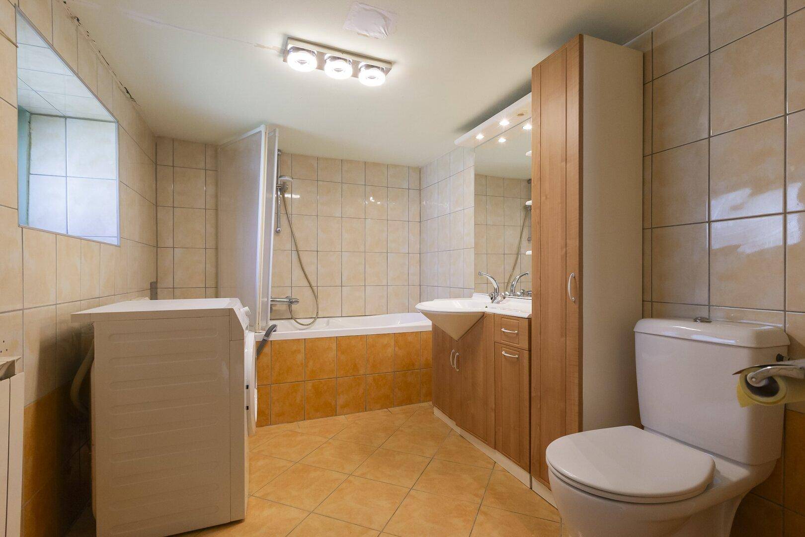 Badezimmer mit beigefarbenen Fliesen, Badewanne mit Duschabtrennung und Waschbecken.