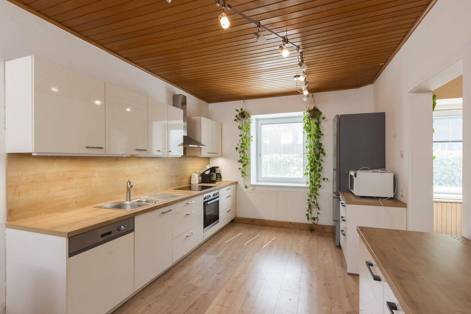 Funktionale Küche mit weißen Hochglanzfronten, Holzdetails und Fenster mit Pflanzen.