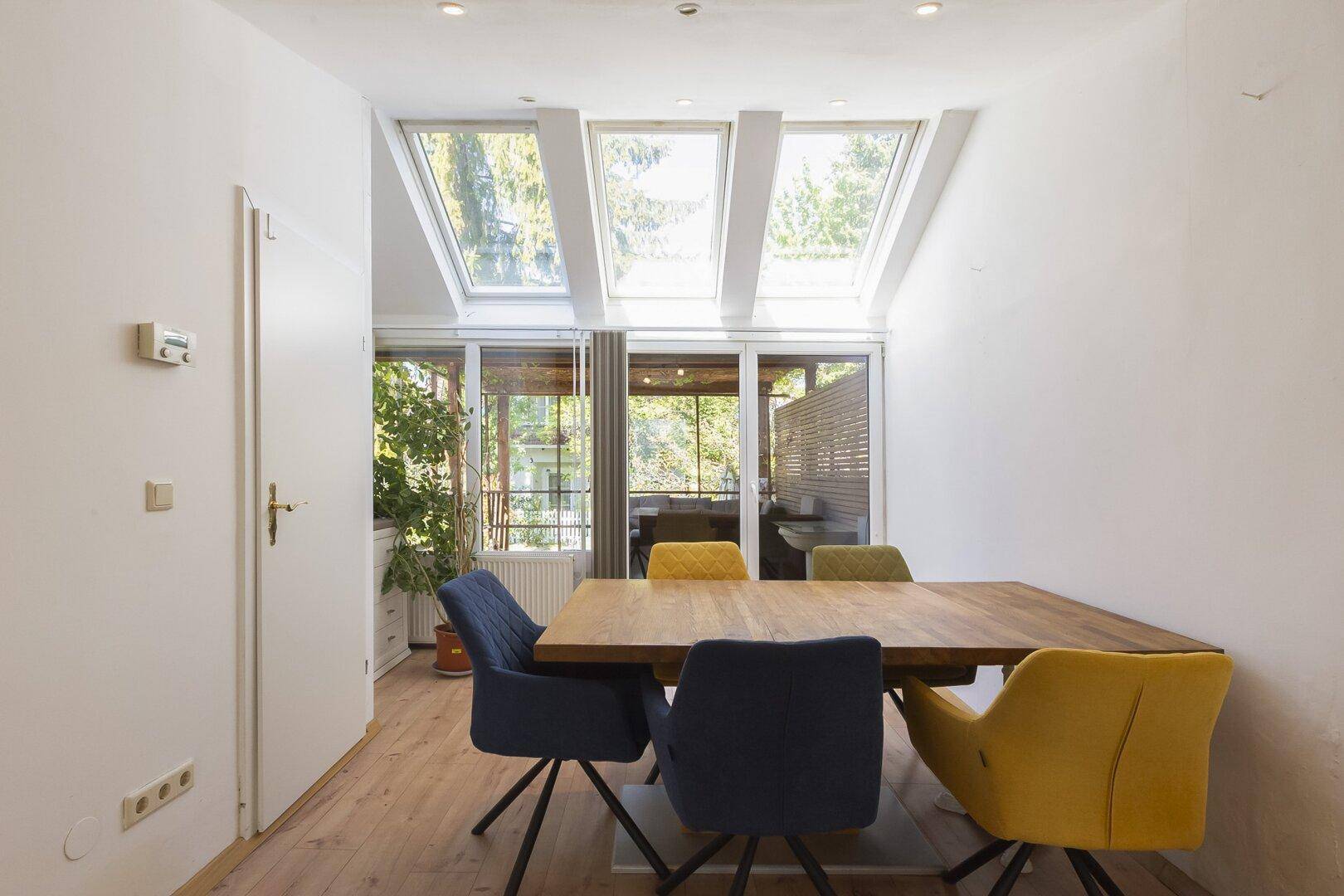 Heller Essbereich mit großem Holztisch und Zugang zur Terrasse durch bodentiefe Fenster.