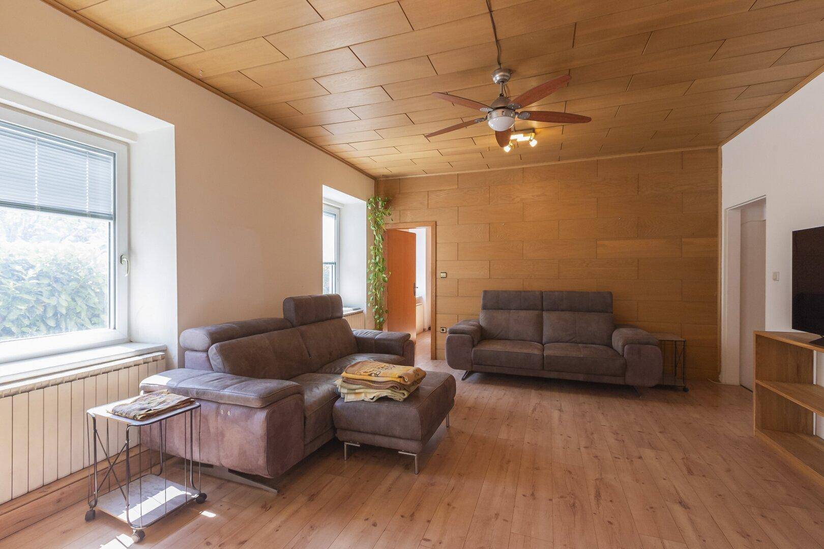 Helles Wohnzimmer mit Holzboden, bequemen Sofas und Blick ins Grüne durch die Fenster.