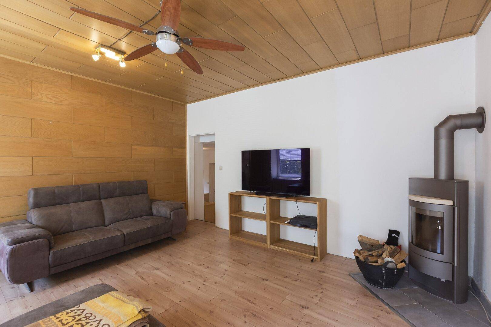 Wohnzimmer mit Holzboden, Deckenventilator und modernem Kaminofen für behagliche Wärme.