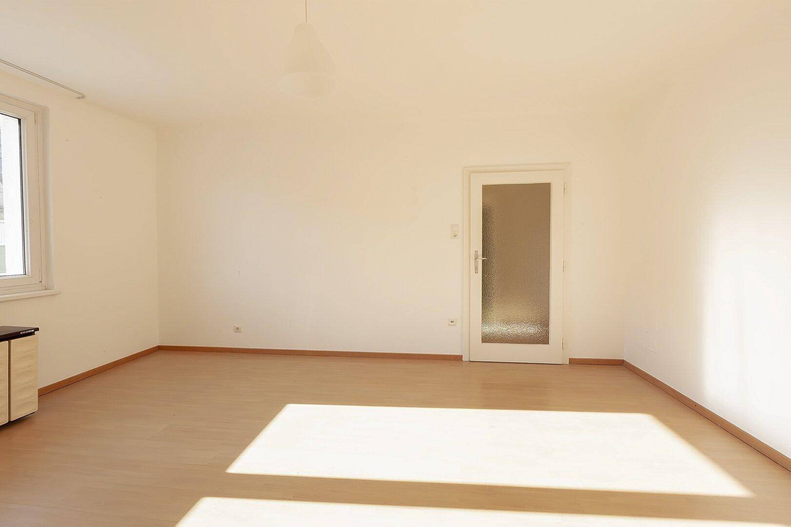Geräumiges, helles Zimmer mit Laminatboden und einer Tür mit Milchglas, die viel Licht spendet.