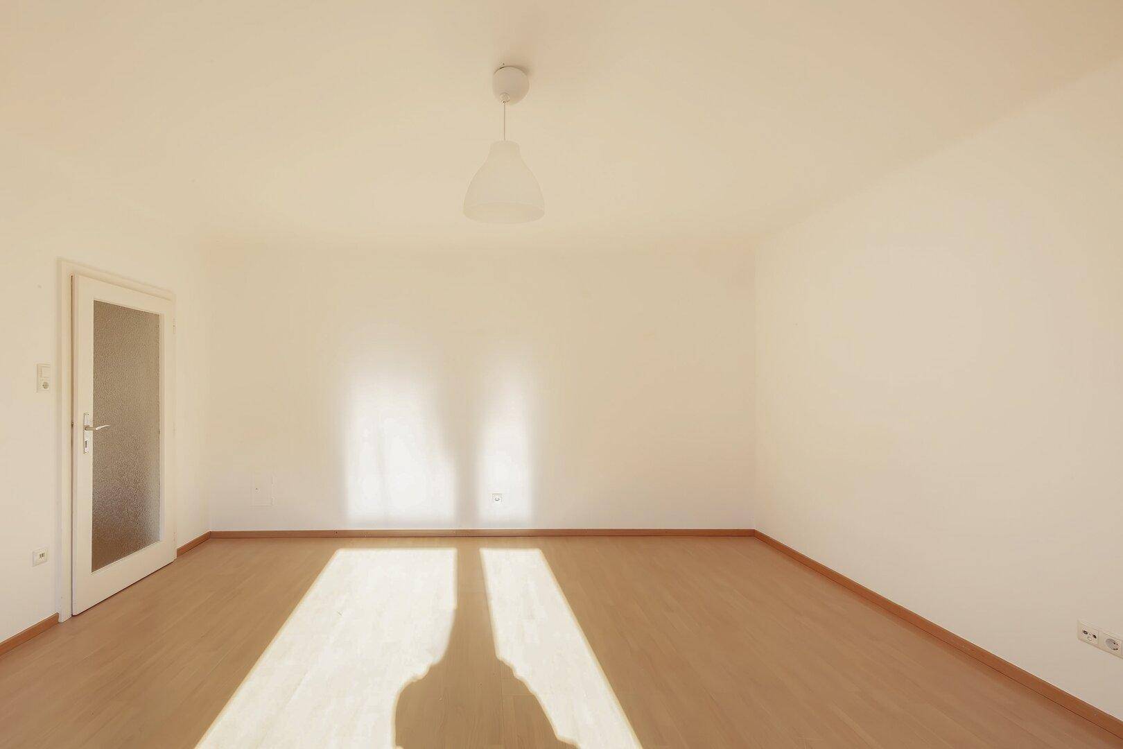 Heller Raum mit Laminatboden und einer Tür, die zu einem weiteren Bereich der Wohnung führt.