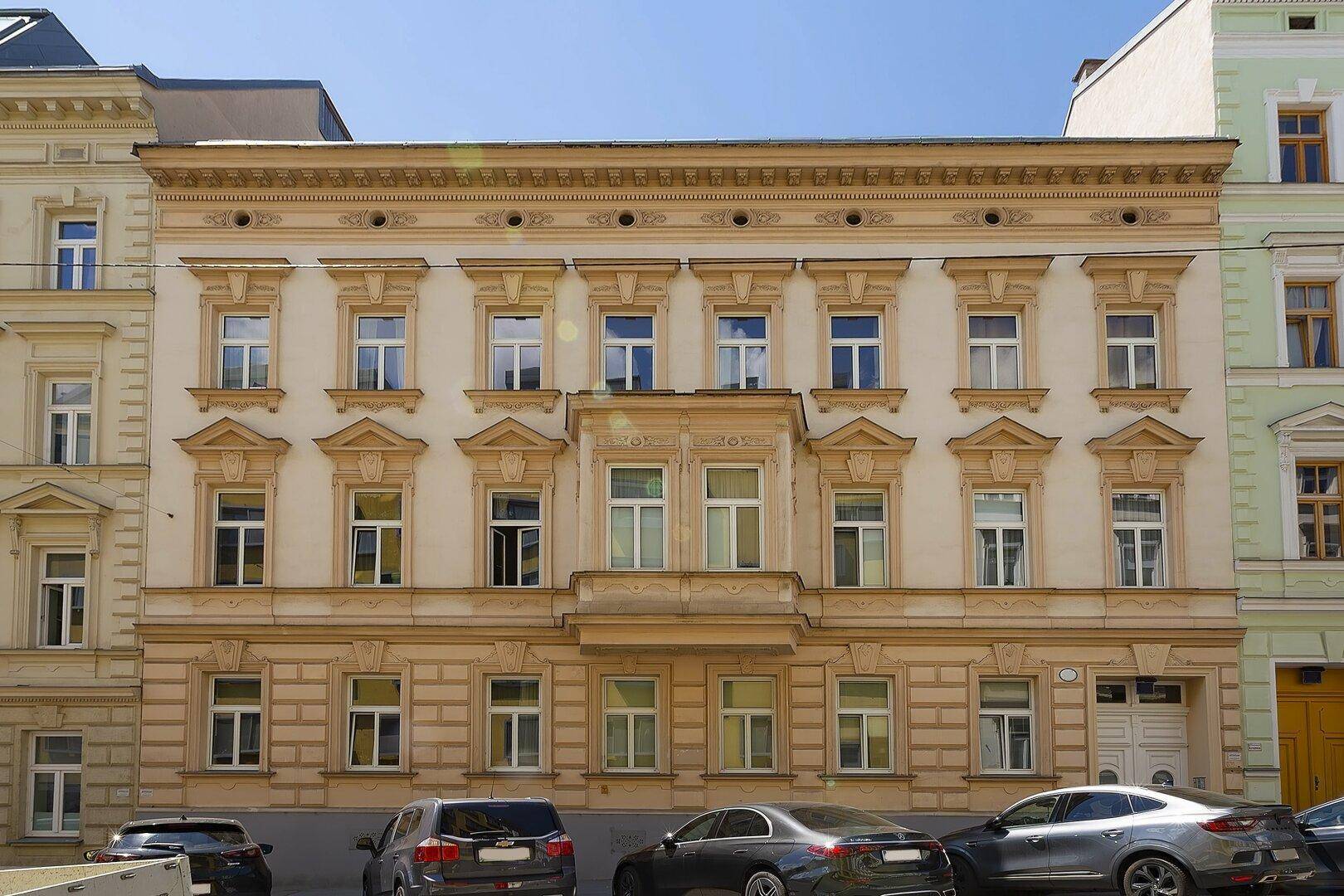Historische Fassade eines Mehrfamilienhauses mit vielen Fenstern und dekorativen Elementen.