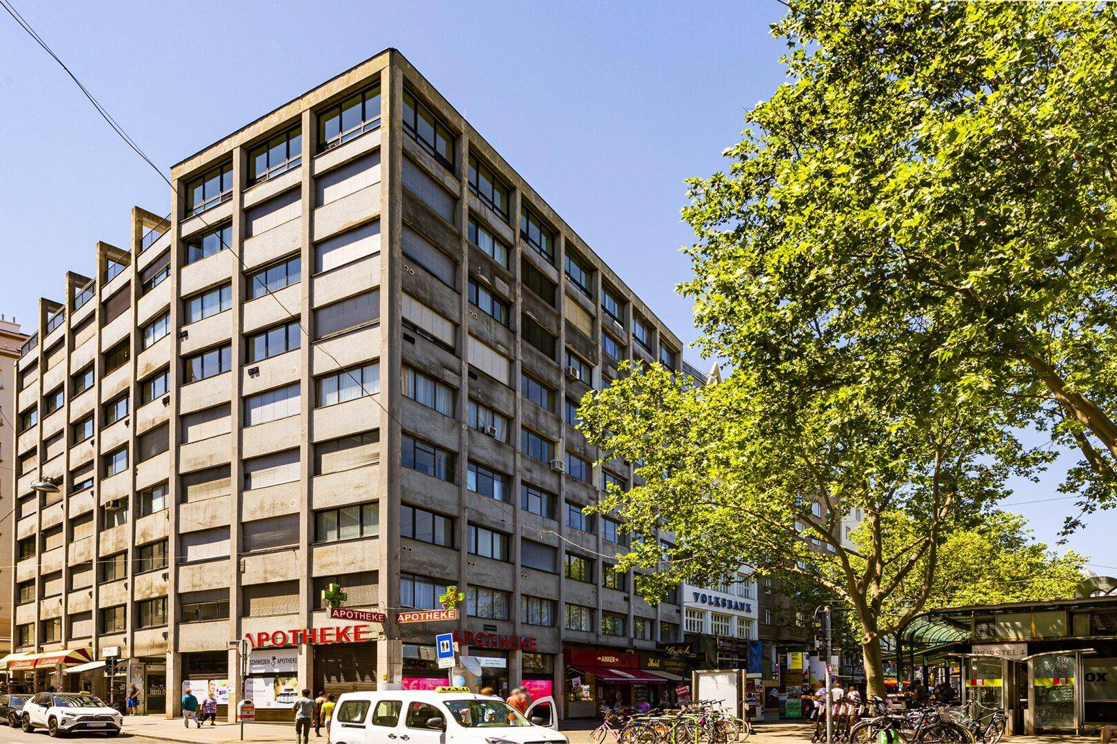 Mehrstöckiges Gebäude mit moderner Betonfassade und großen Fenstern an einer belebten Straße.