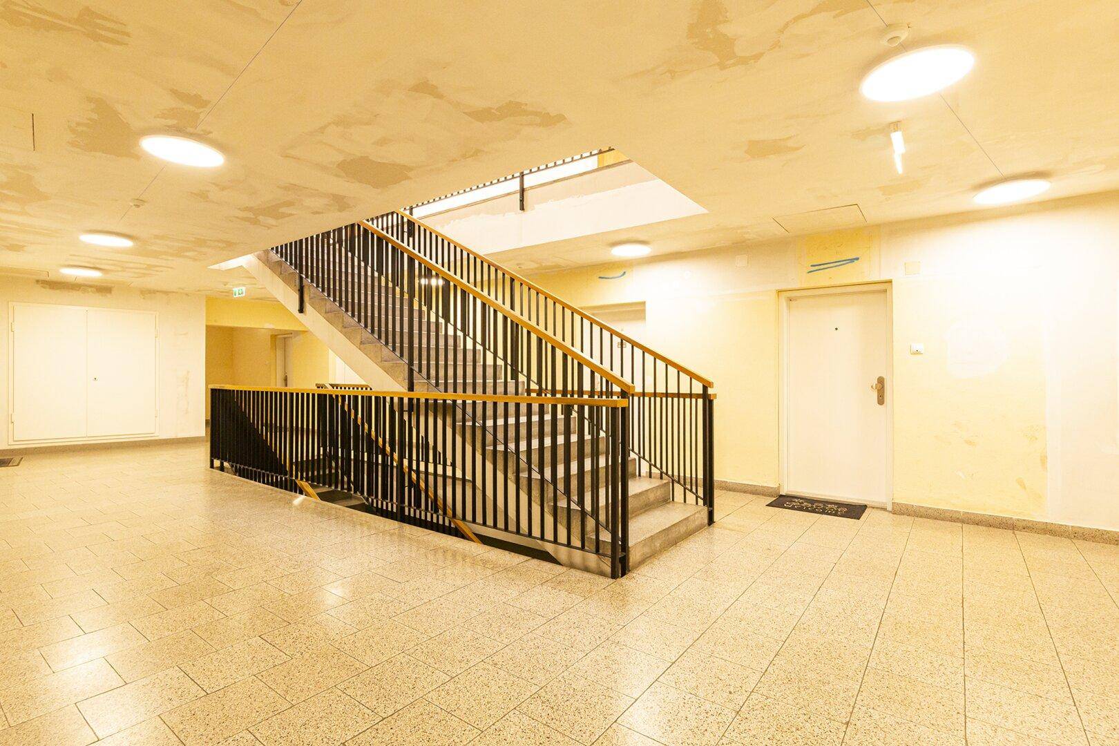 Geräumiger Treppenhausbereich mit Terrazzoboden und Metallgeländer, gut beleuchtet.