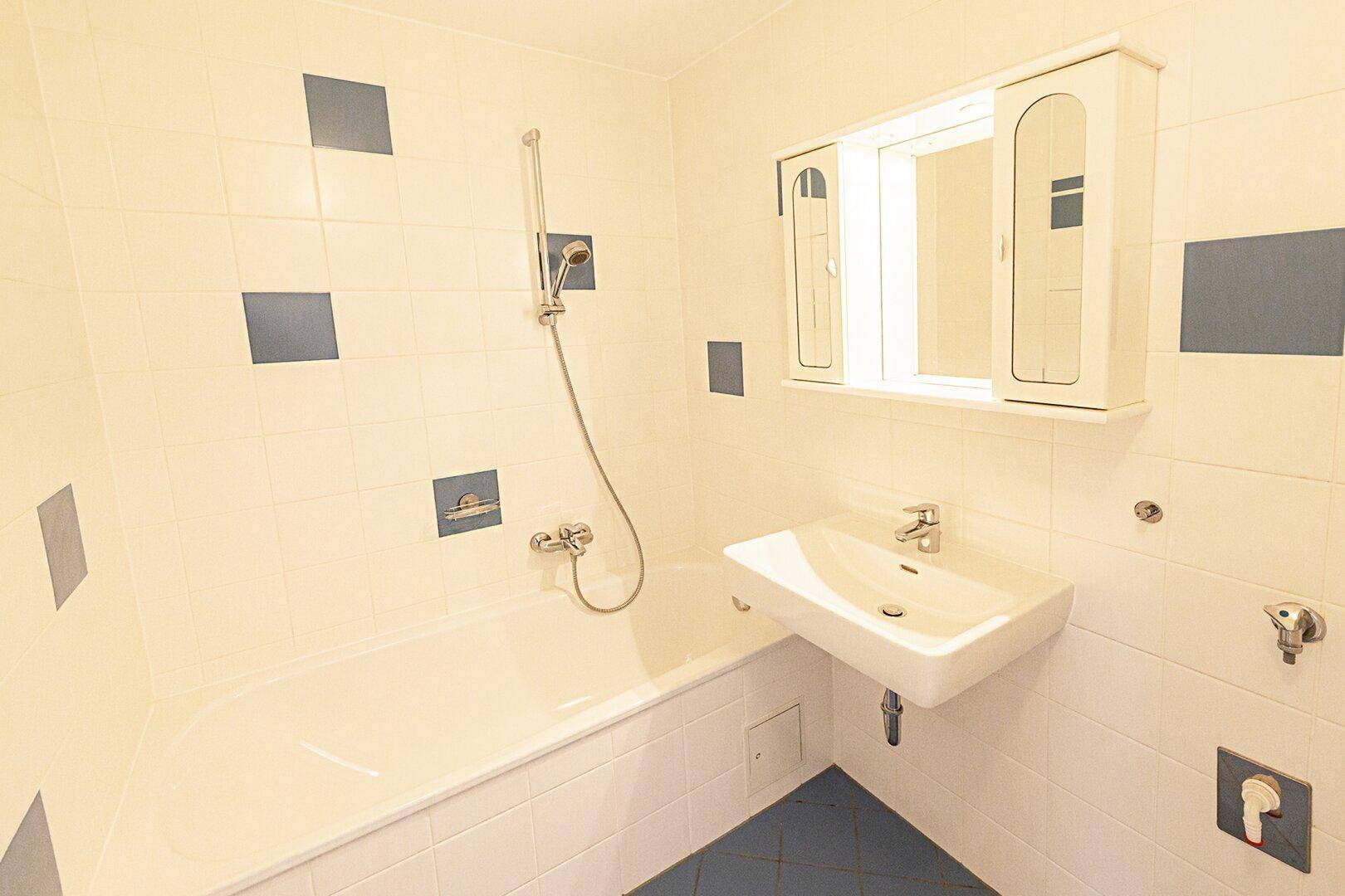 Helles Badezimmer mit Badewanne, Waschbecken und weiß-blauen Fliesen an Wänden und Boden.
