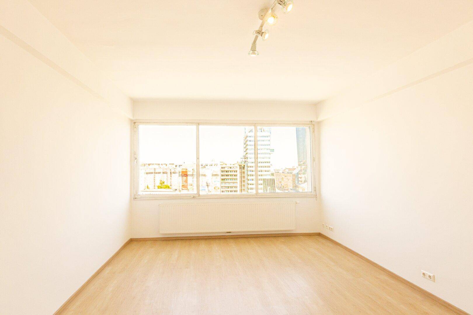 Heller, leerer Raum mit großen Fenstern und Blick auf die Stadt, ausgestattet mit Holzboden.
