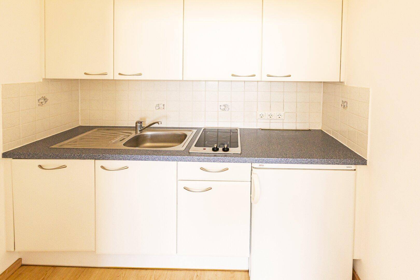 Funktionale Kochnische mit weißen Schränken, Spüle, Kochfeld und kleinem Kühlschrank.