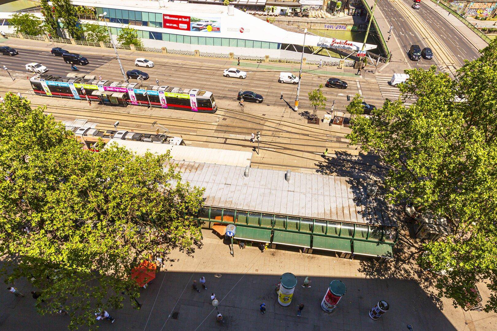Vogelperspektive einer belebten Stadtstraße mit Straßenbahnen, Autos und vielen Bäumen.