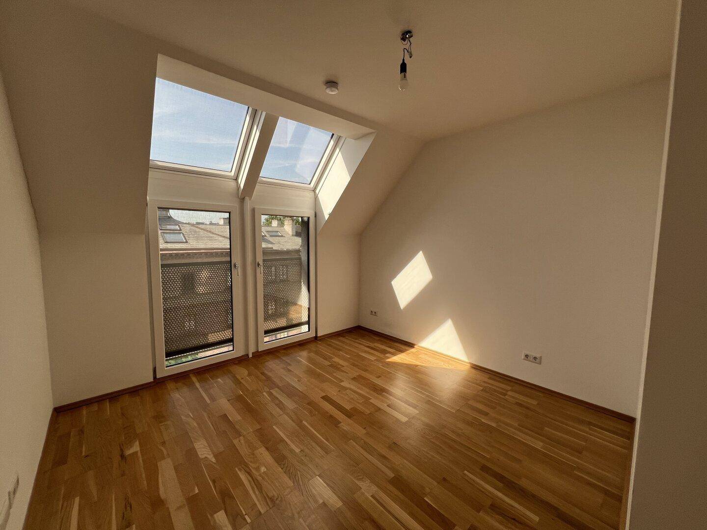 Helles Zimmer mit Holzboden und großen Dachfenstern, die viel Tageslicht hereinlassen.