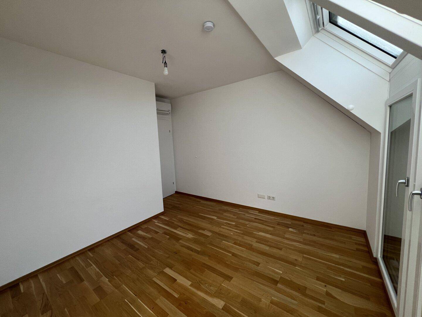 Geräumiges Zimmer mit Holzboden, Dachfenster und Klimaanlage für angenehmes Raumklima.