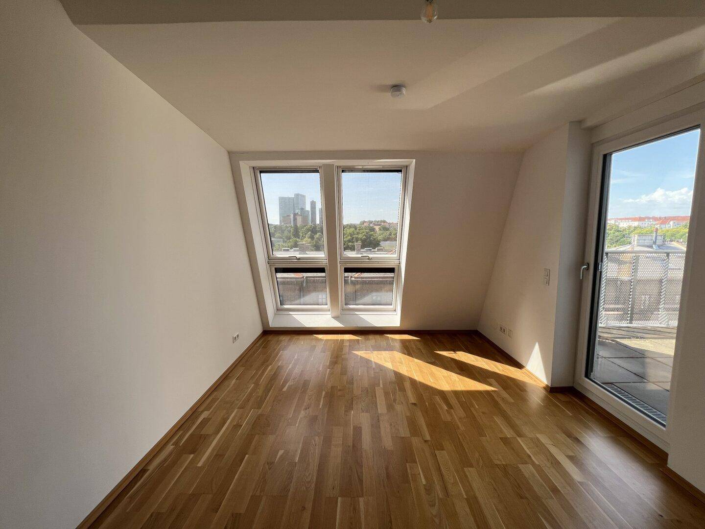 Lichtdurchflutetes Zimmer mit Holzboden und großen Fenstern mit Stadtblick.