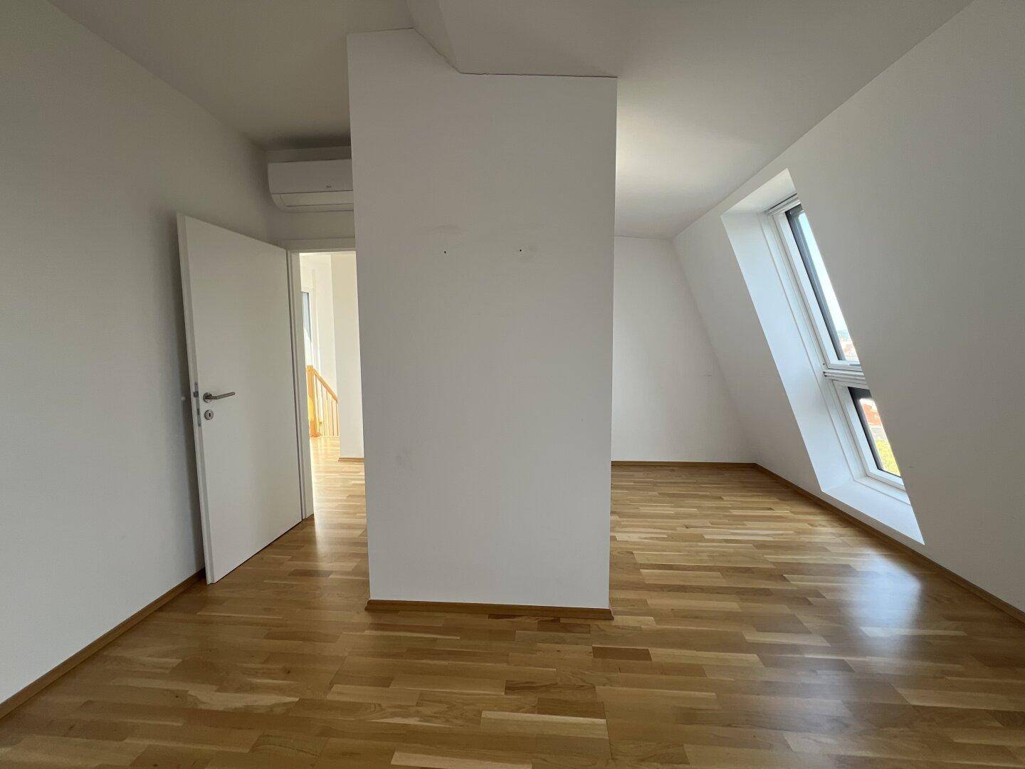 Helles Zimmer mit Holzboden, weißer Wand und Klimaanlage.