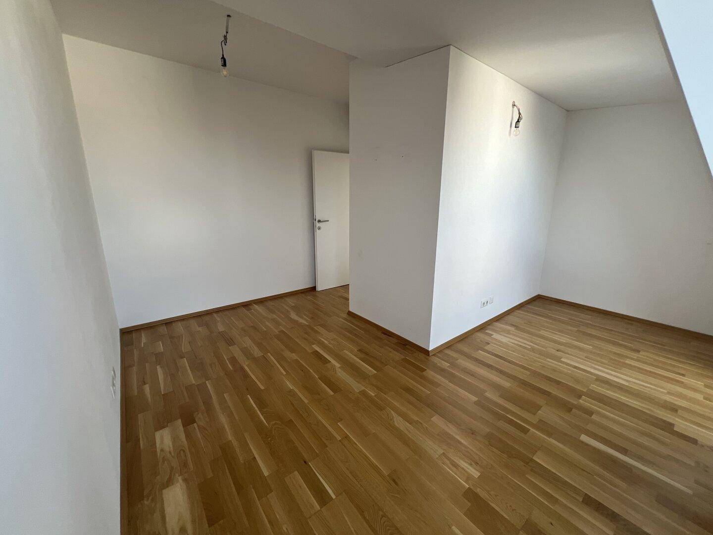 Geräumiges Zimmer mit Holzboden und weiß gestrichenen Wänden.