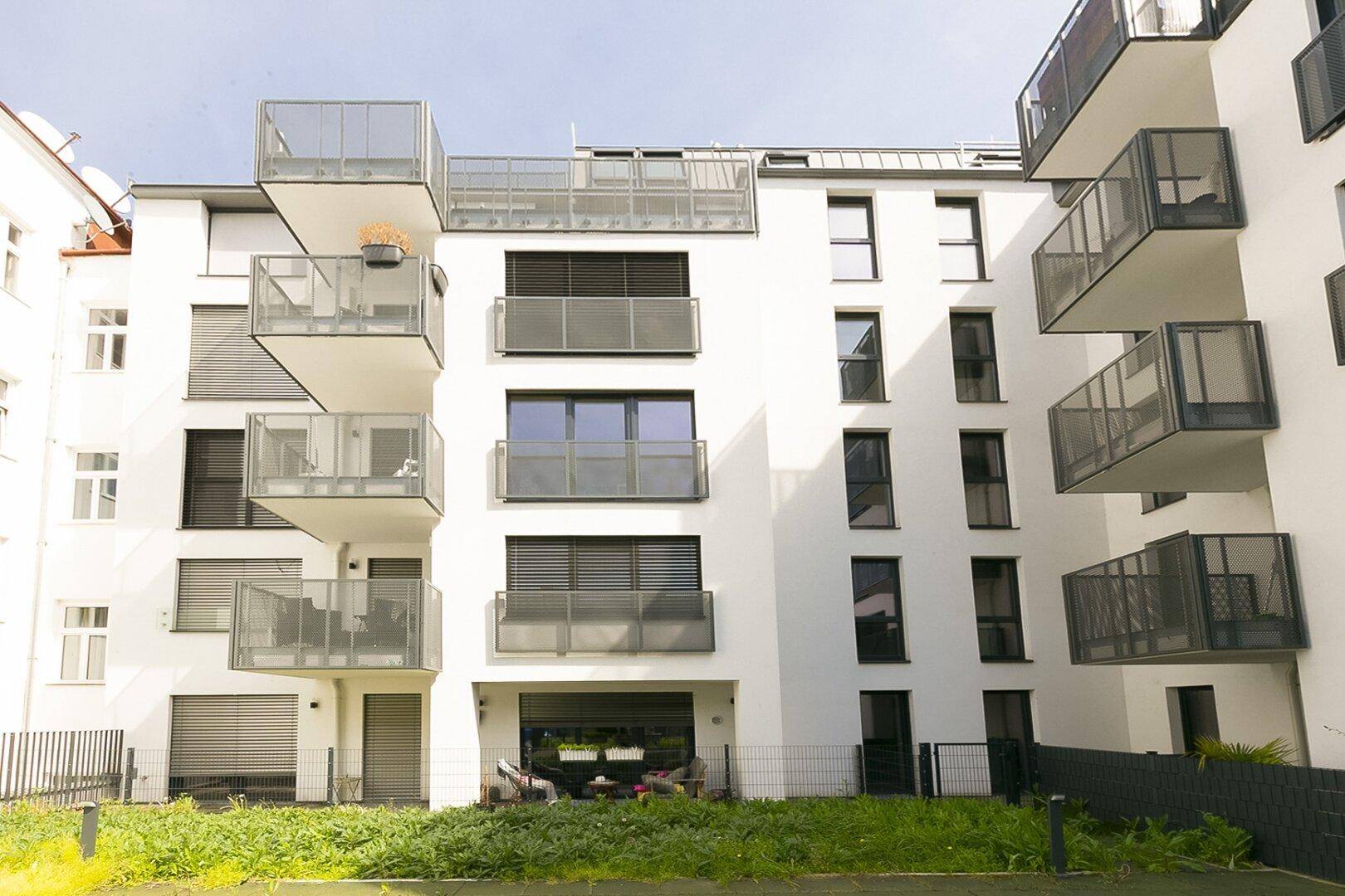 Moderne Gebäudefassade mit Balkonen, Terrassen und einem kleinen Gartenbereich.