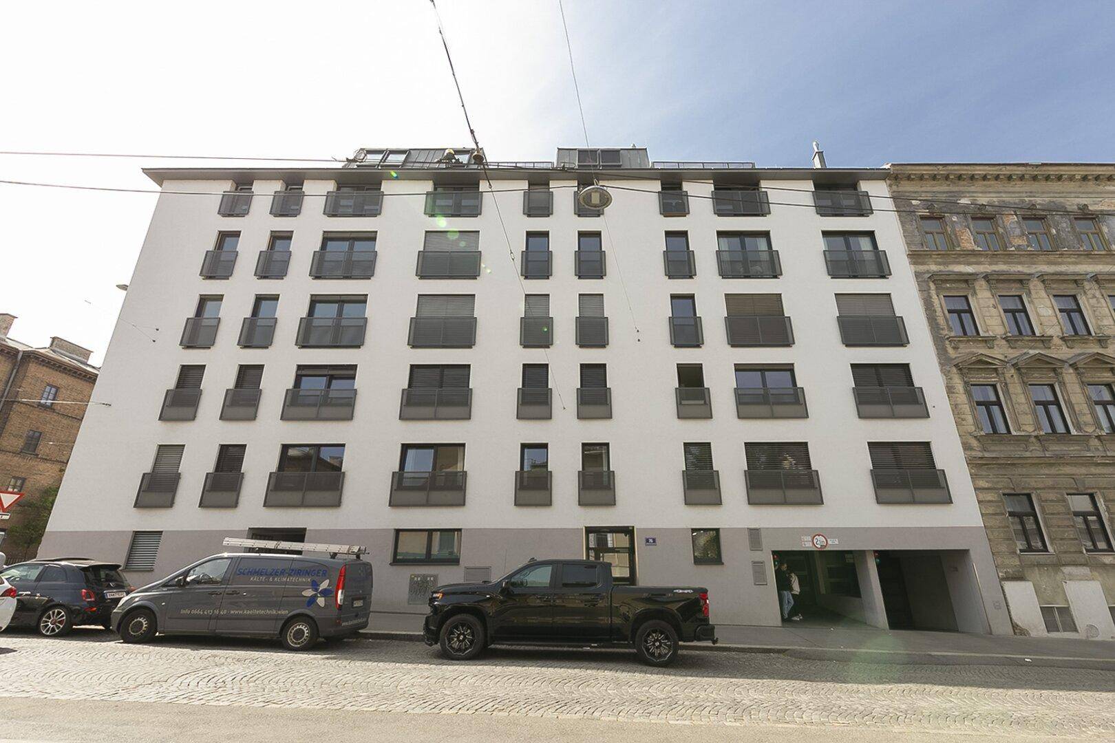 Moderne Wohnhausfassade von der Straße aus gesehen mit vielen Fenstern und Balkonen.
