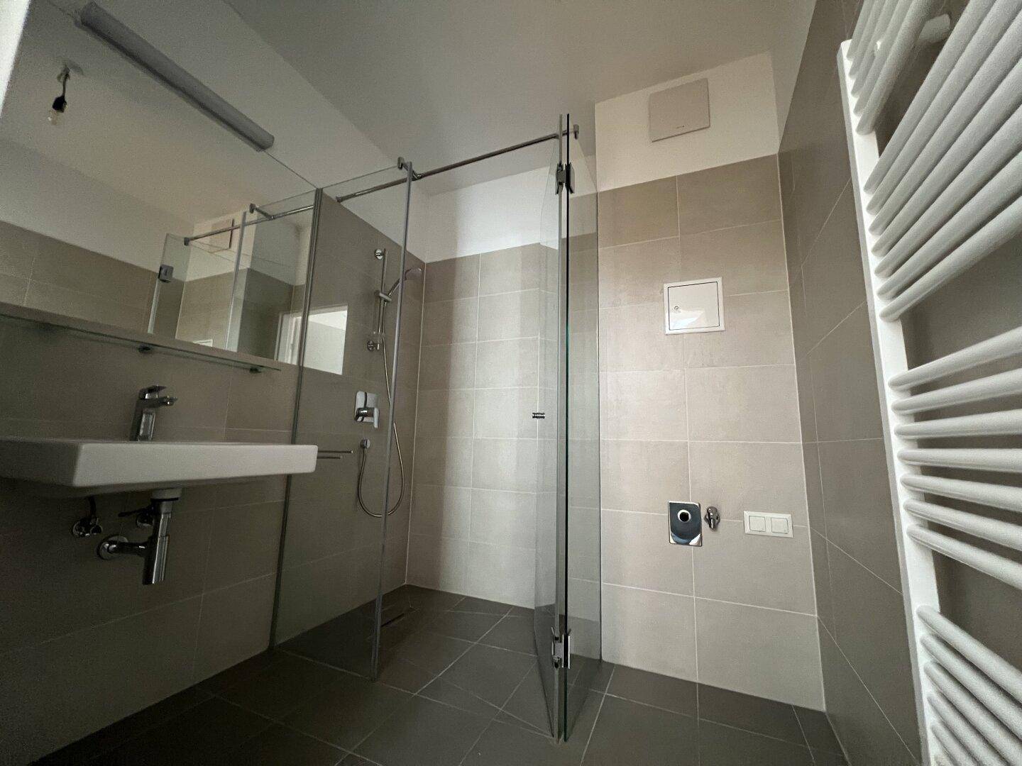 Modernes Badezimmer mit begehbarer Dusche, grauen Fliesen und beheiztem Handtuchhalter.