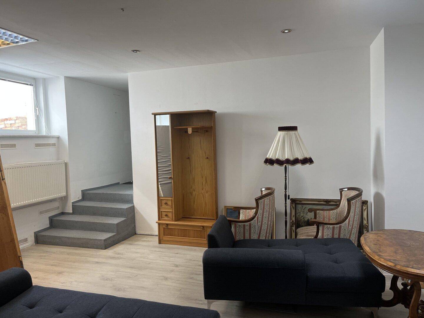 Ein gemütlicher Wohnbereich mit dunklem Sofa, Holzmöbeln und einer Stehlampe.
